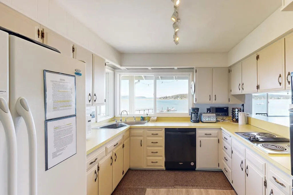 Una cocina luminosa con encimeras y armarios alrededor de una ventana con vista al agua.