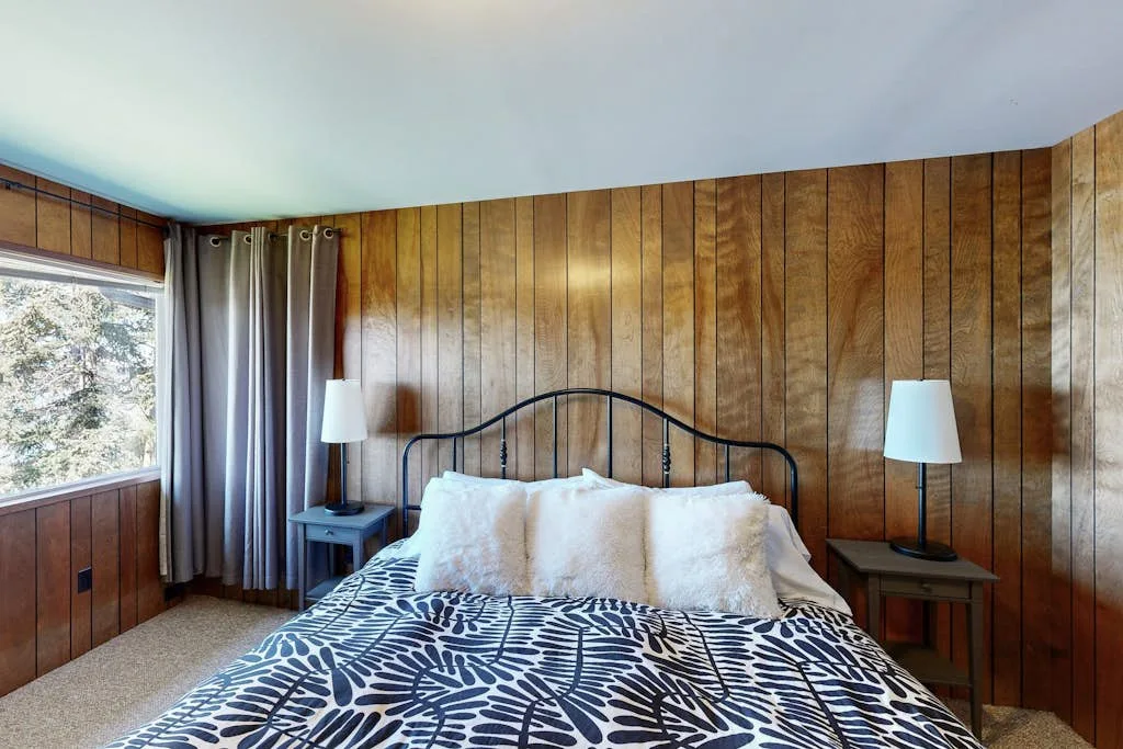 Un dormitorio con una cama, ropa de cama estampada y paredes revestidas de madera.