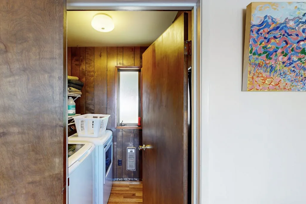 Un cuarto de lavandería estrecho con lavadora y secadora bajo una ventana pequeña.