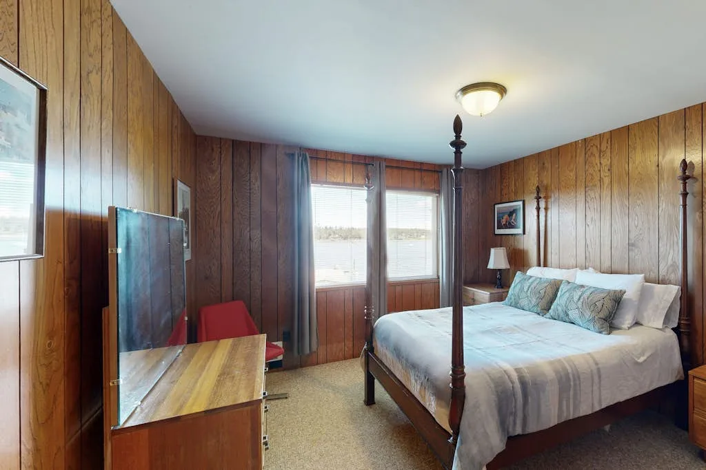 Dormitorio con paredes revestidas de madera, una cama y un televisor.