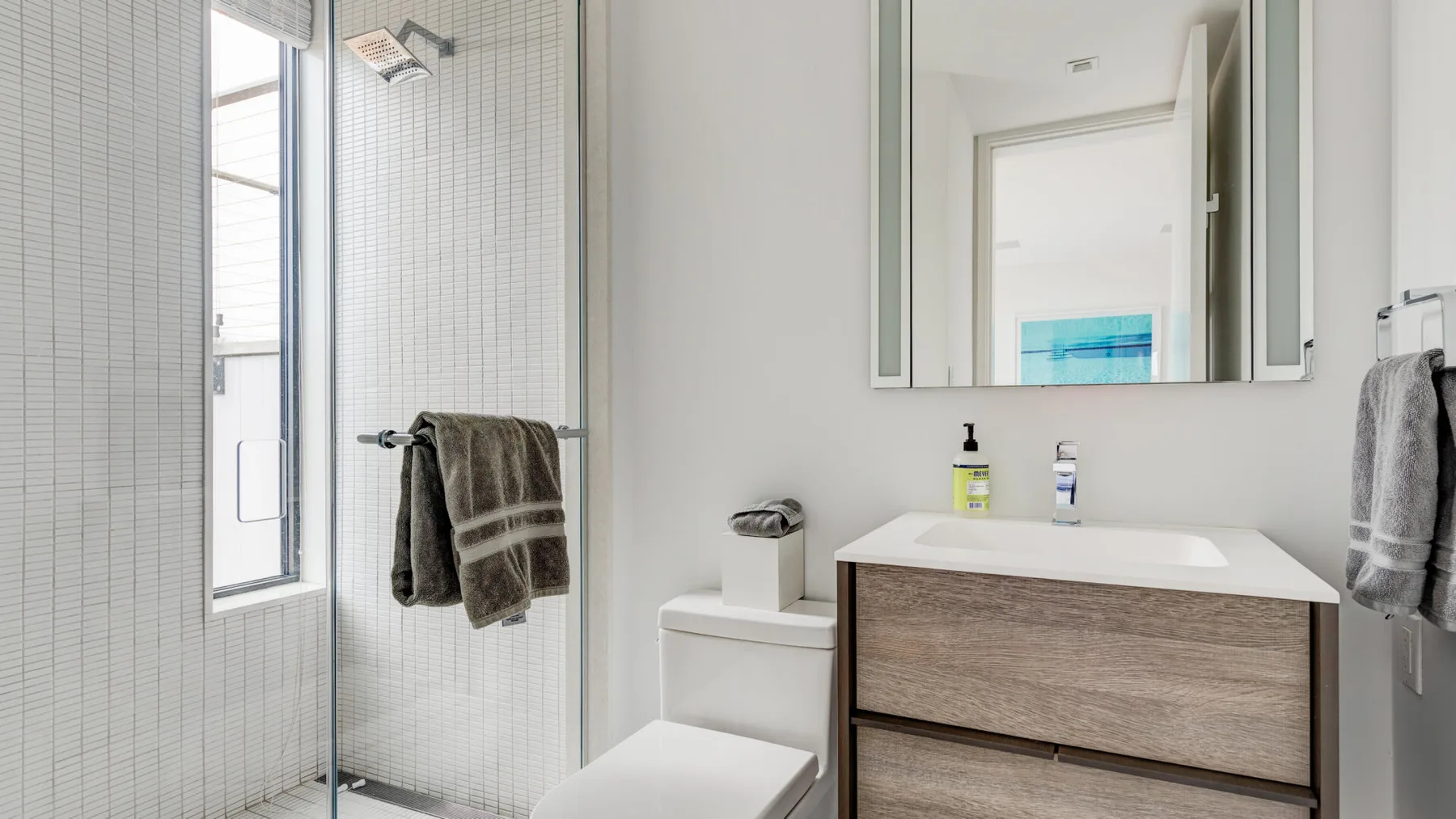 A bright bathroom with a vanity, mirror, and glass shower.