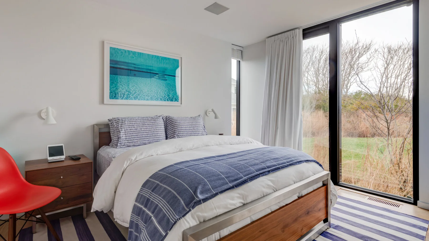 A bedroom with a neatly made bed beside large windows overlooking a garden.