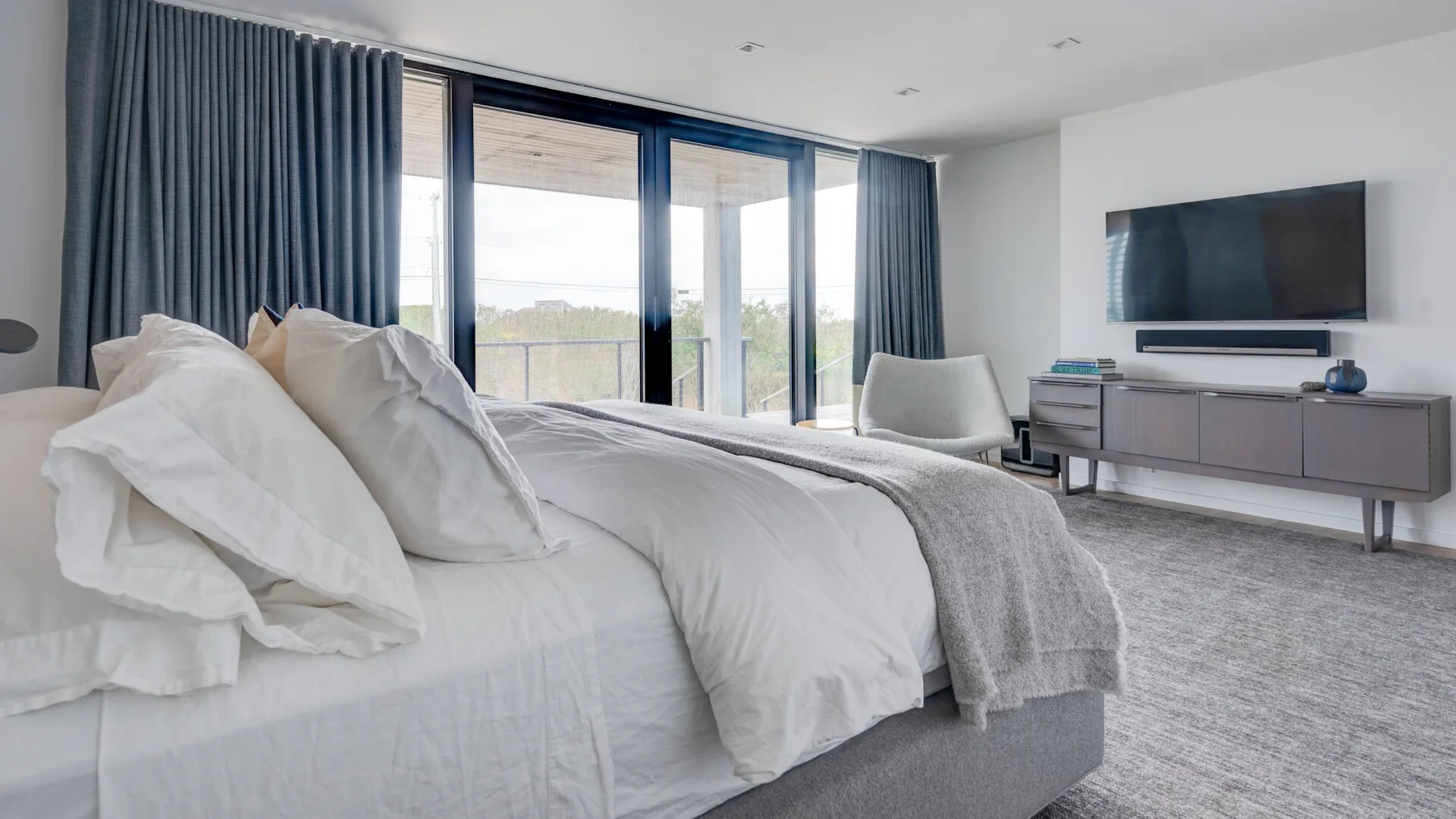 A bright bedroom with a bed, large windows, and a television.