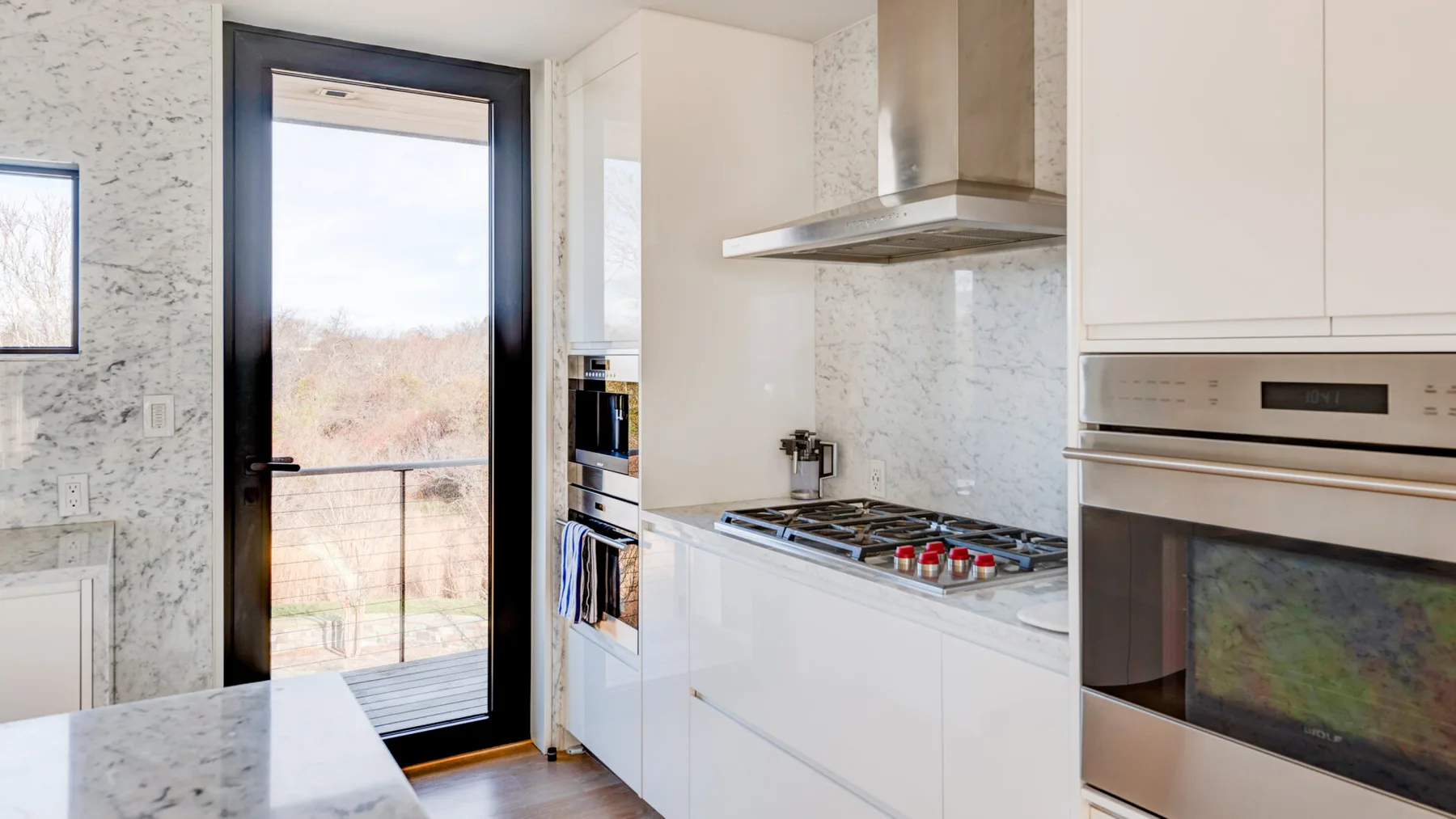 A bright modern kitchen with white cabinetry and a glass door.