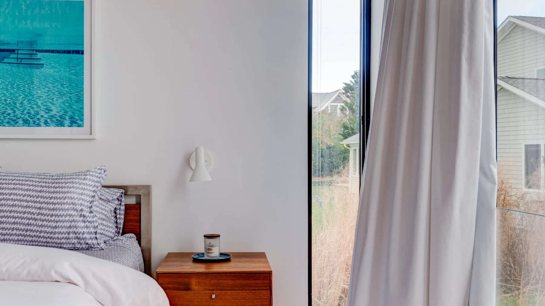 A bedroom with a bed beside a wooden nightstand and a curtained window.
