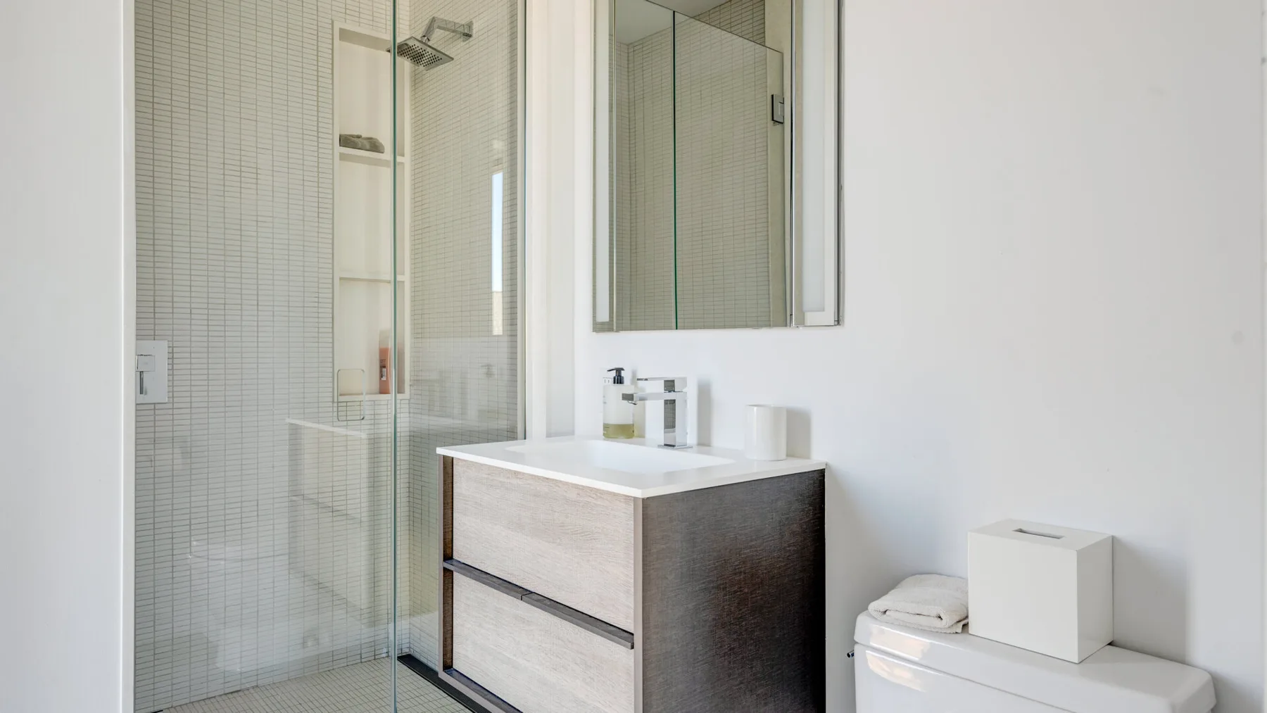 A bright bathroom with a glass shower and a vanity.
