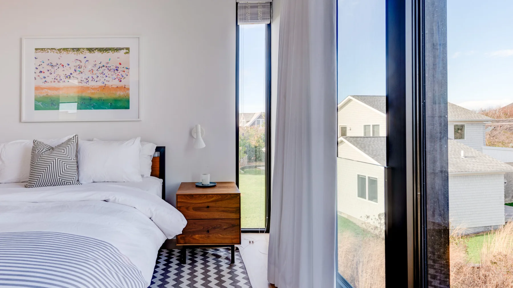 A bright bedroom with a neatly made bed beside tall windows.