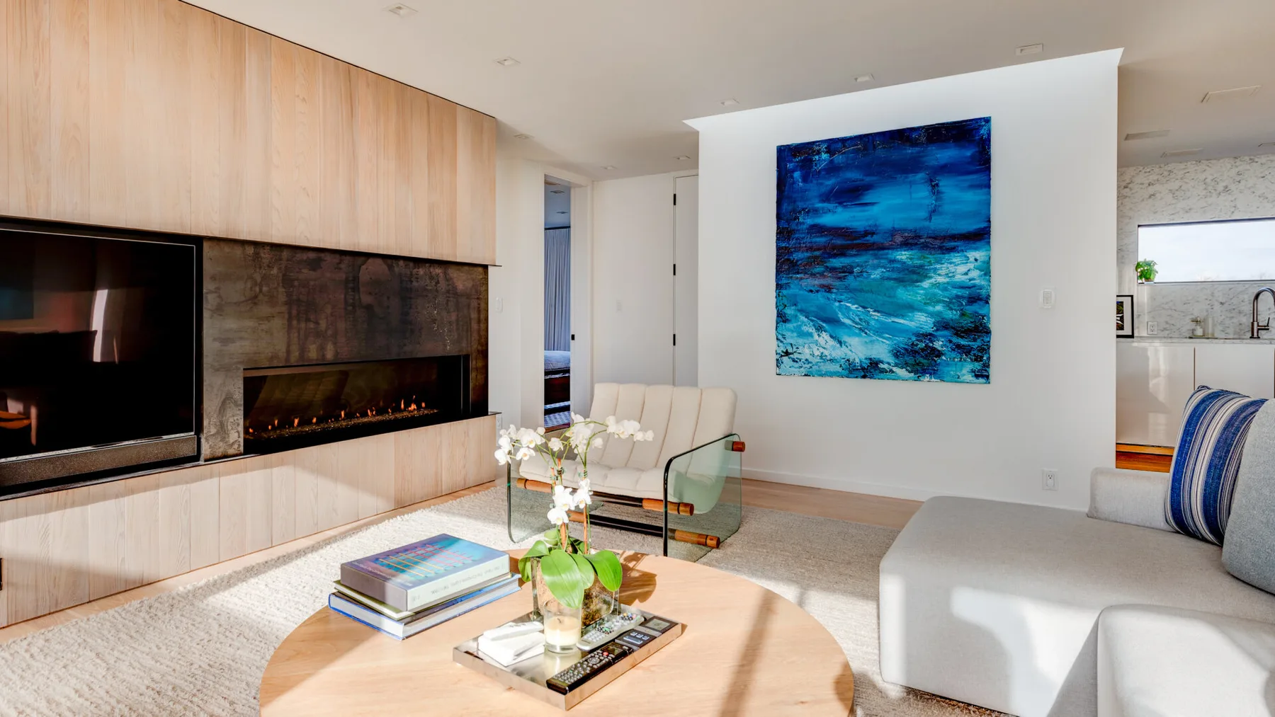 A bright living room with a fireplace, seating, and a large blue painting.