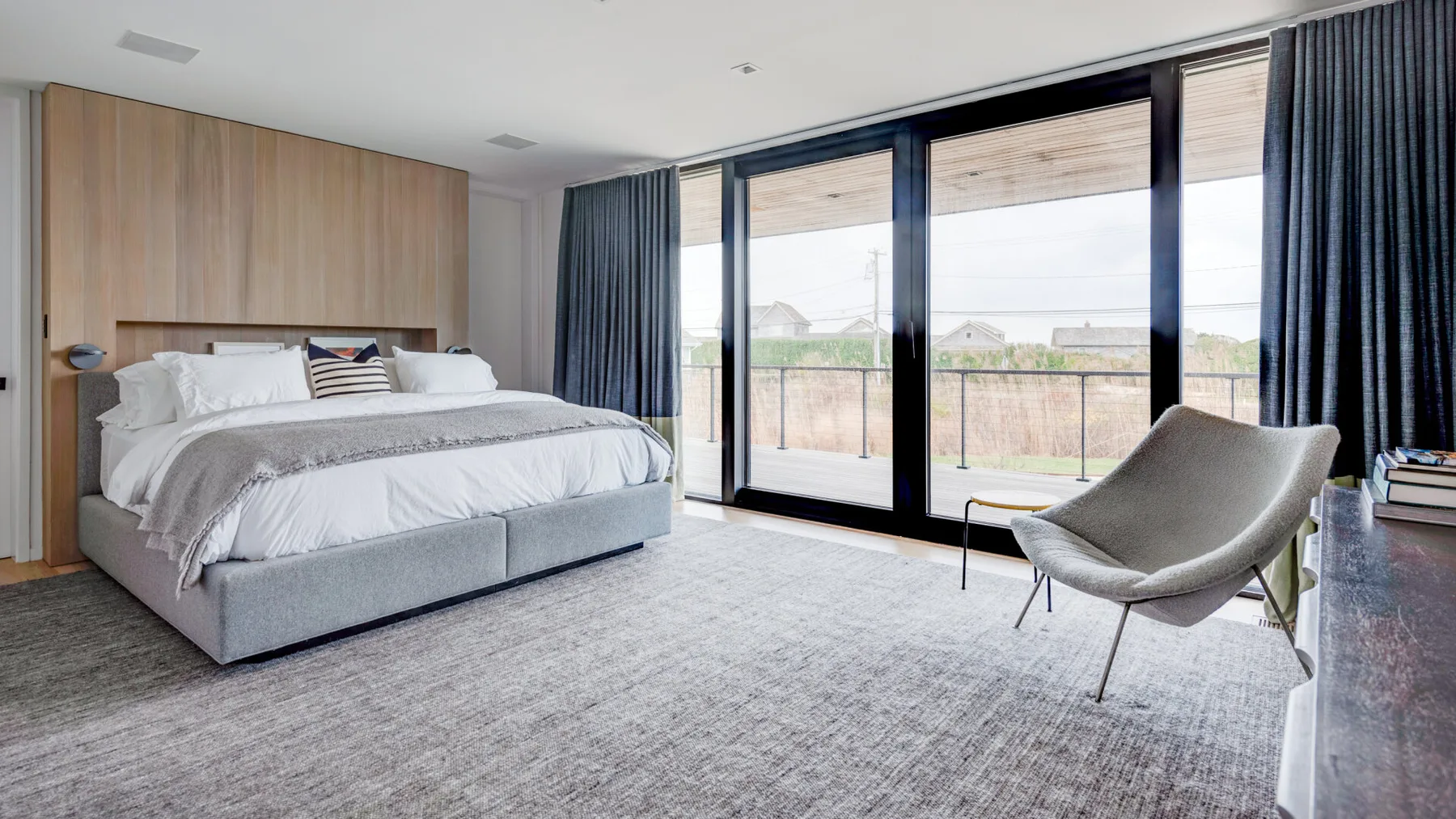 A bedroom with a large bed, floor-to-ceiling windows, and a lounge chair.