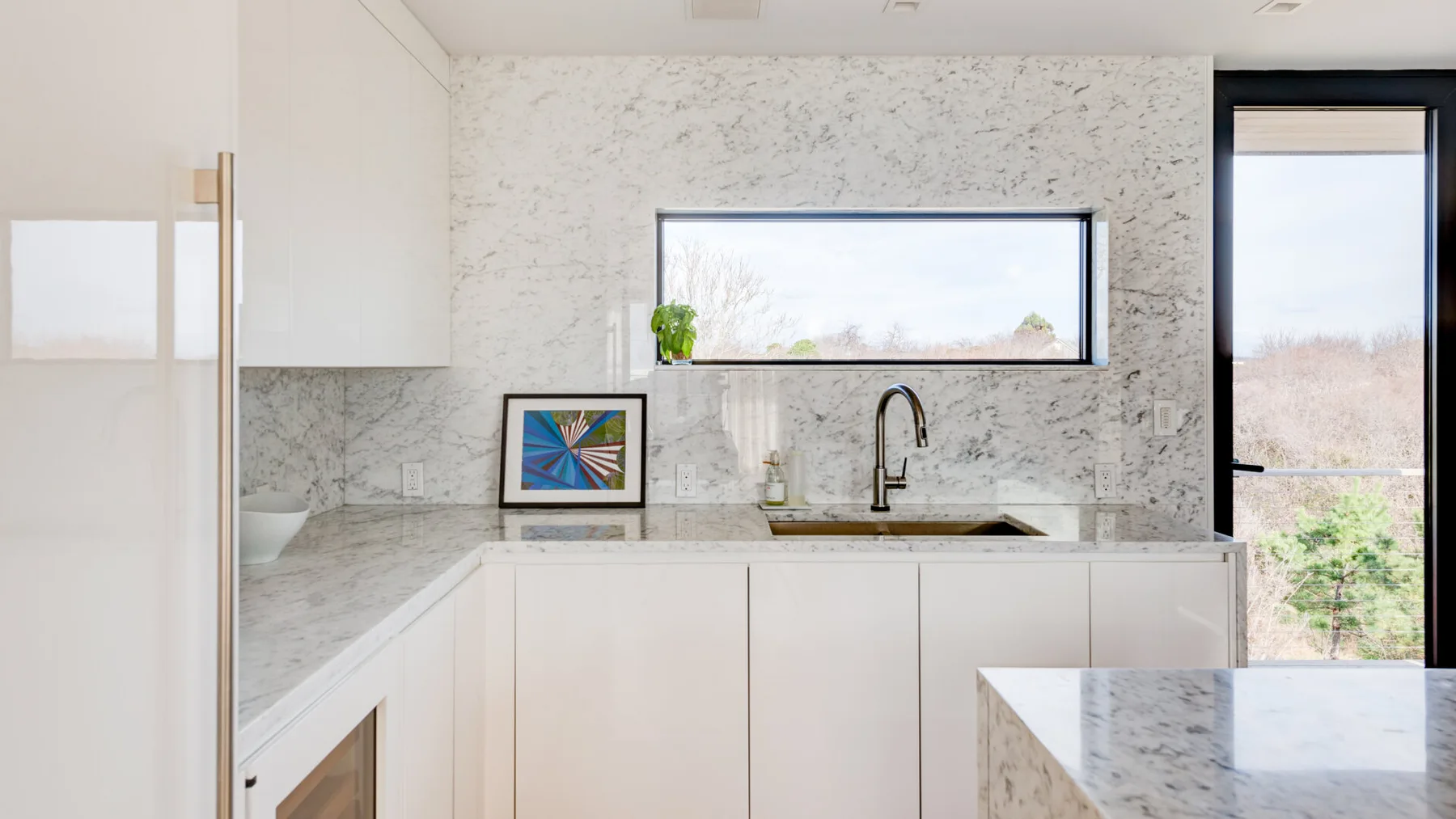 A bright modern kitchen with white cabinetry and a marble-patterned countertop.