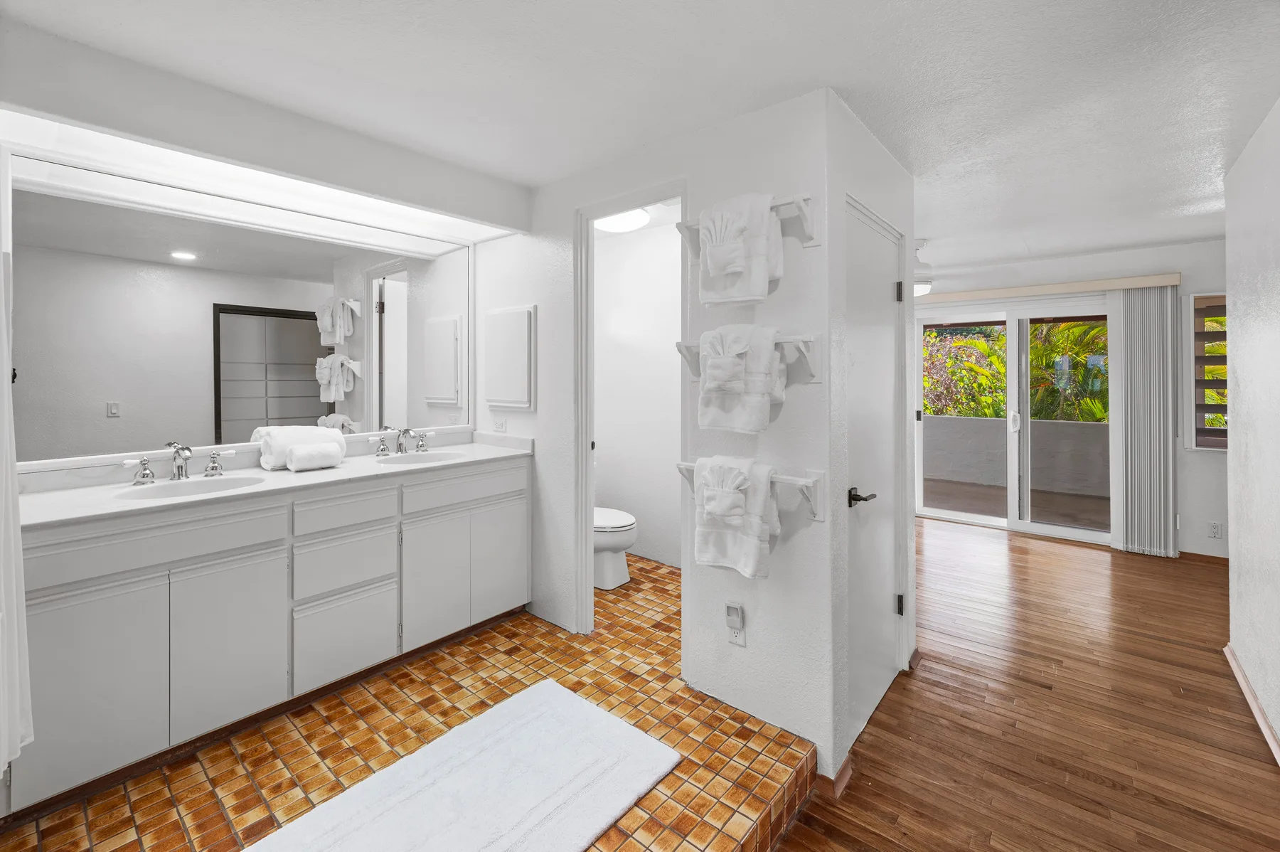 A bathroom with a long vanity and a doorway opening onto a bright room.