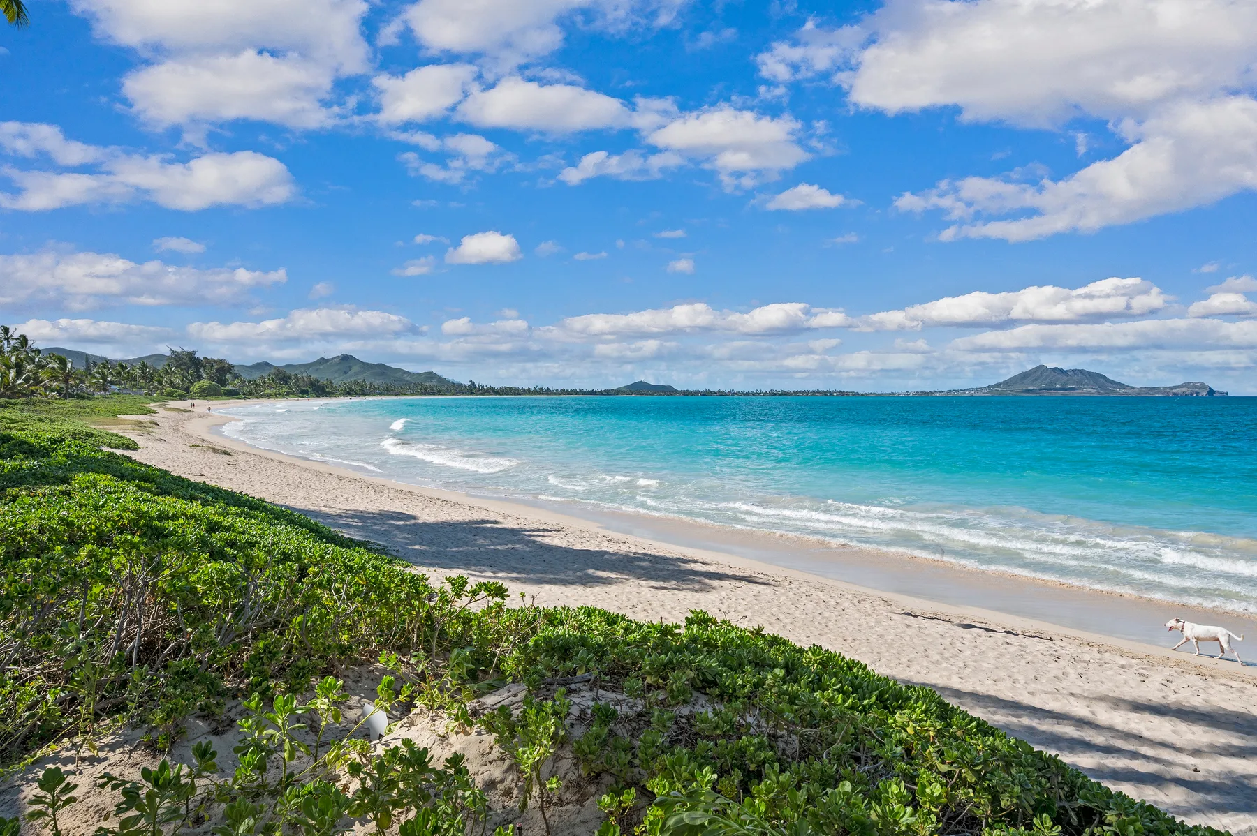 A curved sandy beach borders turquoise water beneath a partly cloudy sky.
