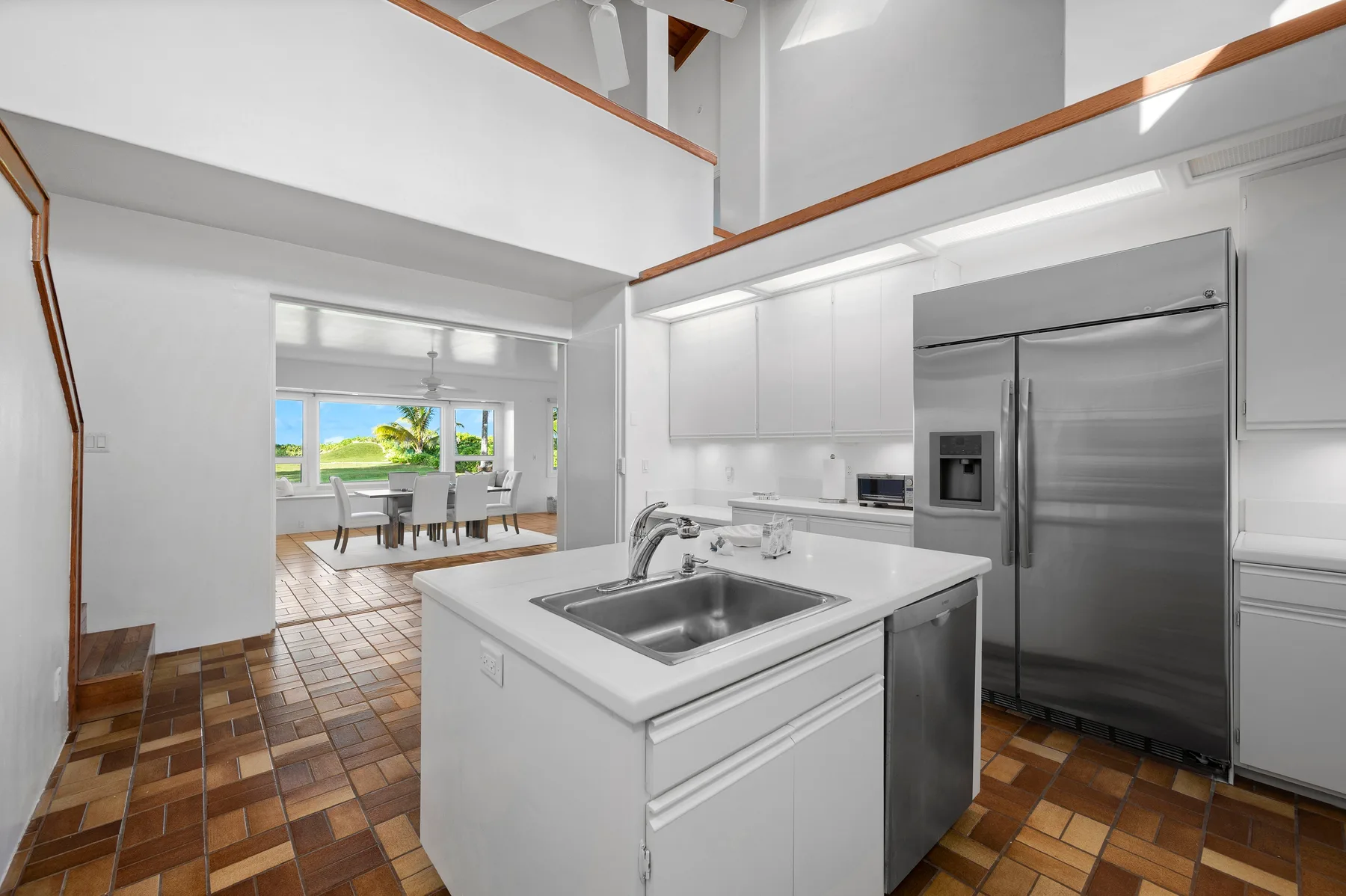 A bright kitchen with a central island and stainless steel refrigerator.