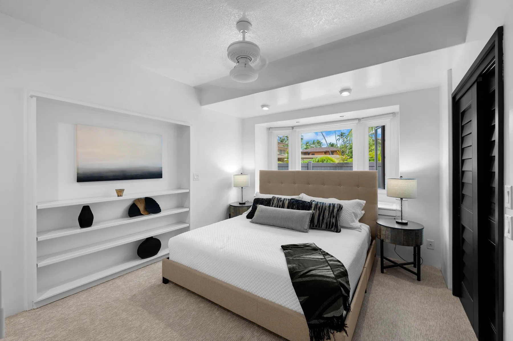 A bright bedroom features a bed between built-in shelves and bedside tables.
