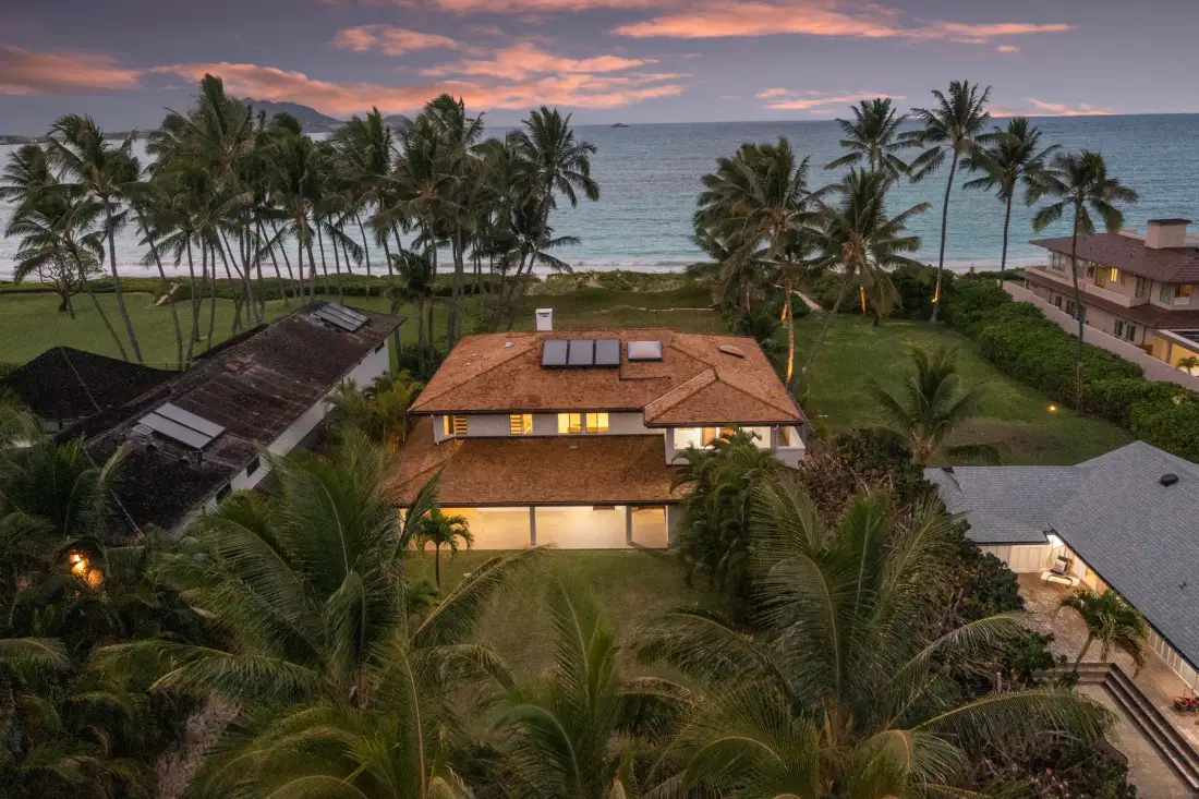 A coastal property surrounded by palm trees overlooks the ocean at sunset.
