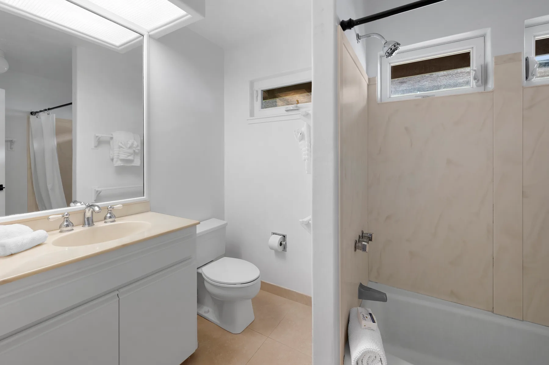 A bright bathroom with a vanity, toilet, and bathtub with a shower.