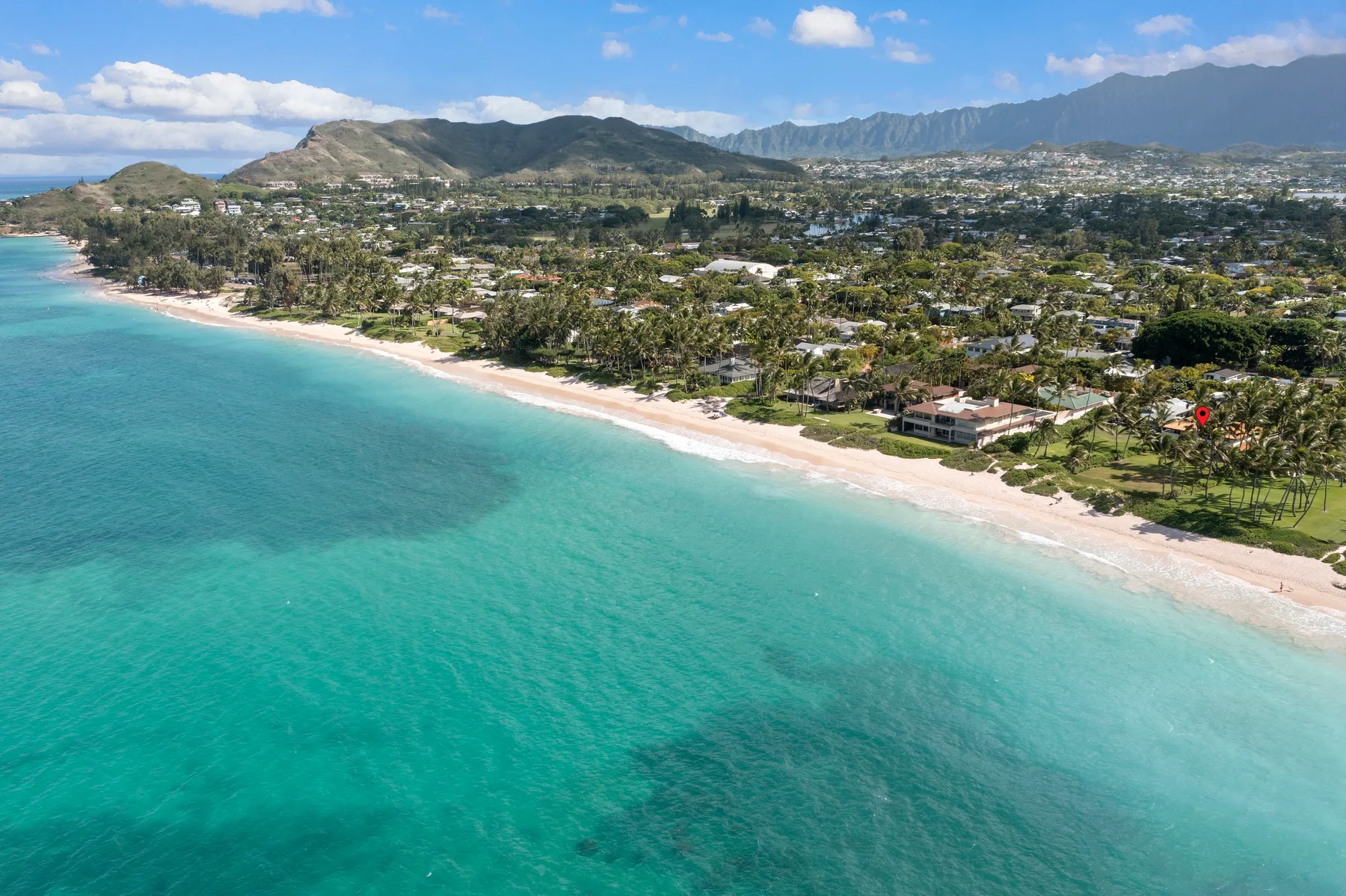 Aerial view of a tropical coastline with turquoise water, a sandy beach, and homes along shore.