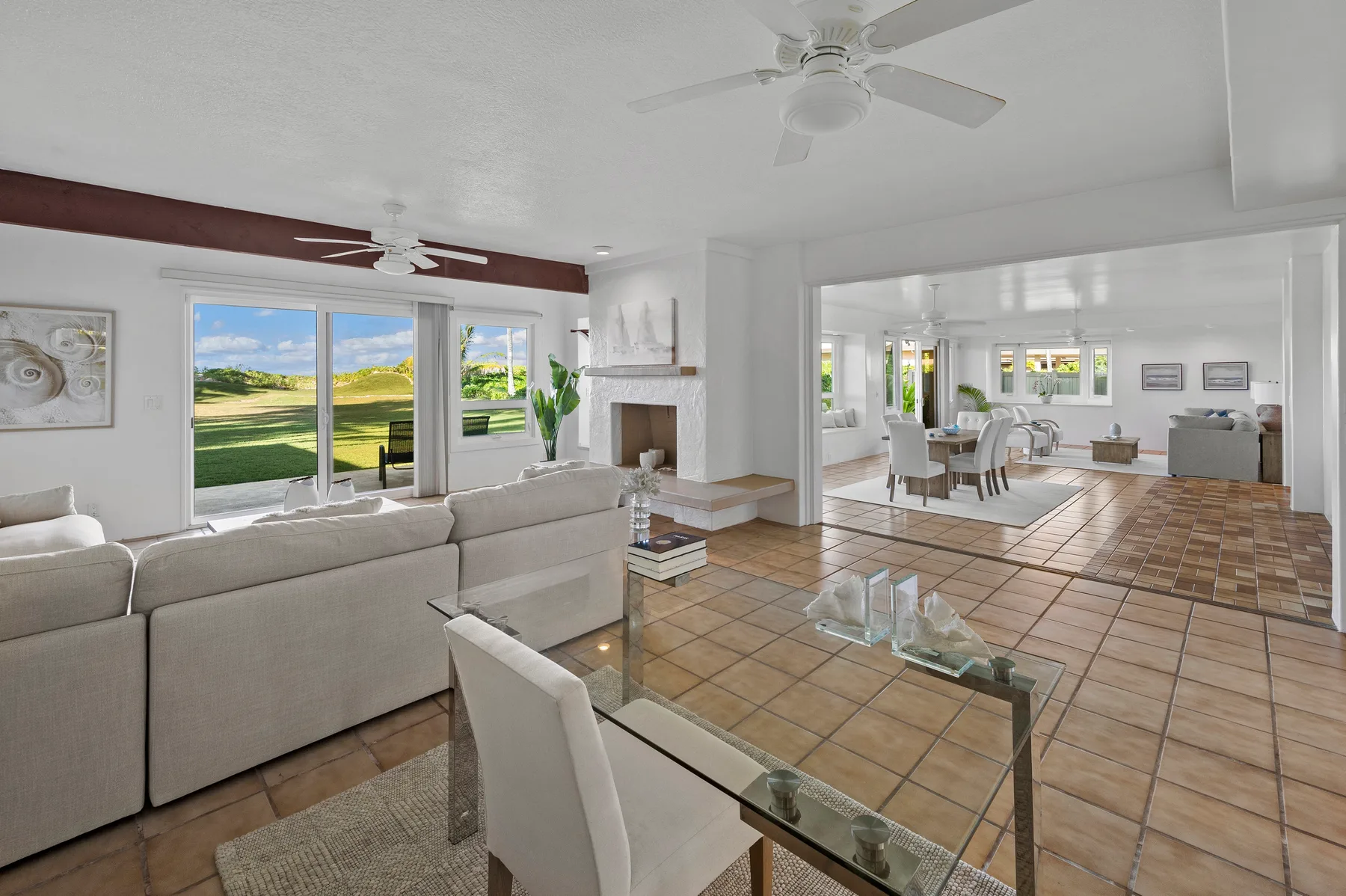 A bright living room opens into a dining area, with large windows overlooking a green lawn.