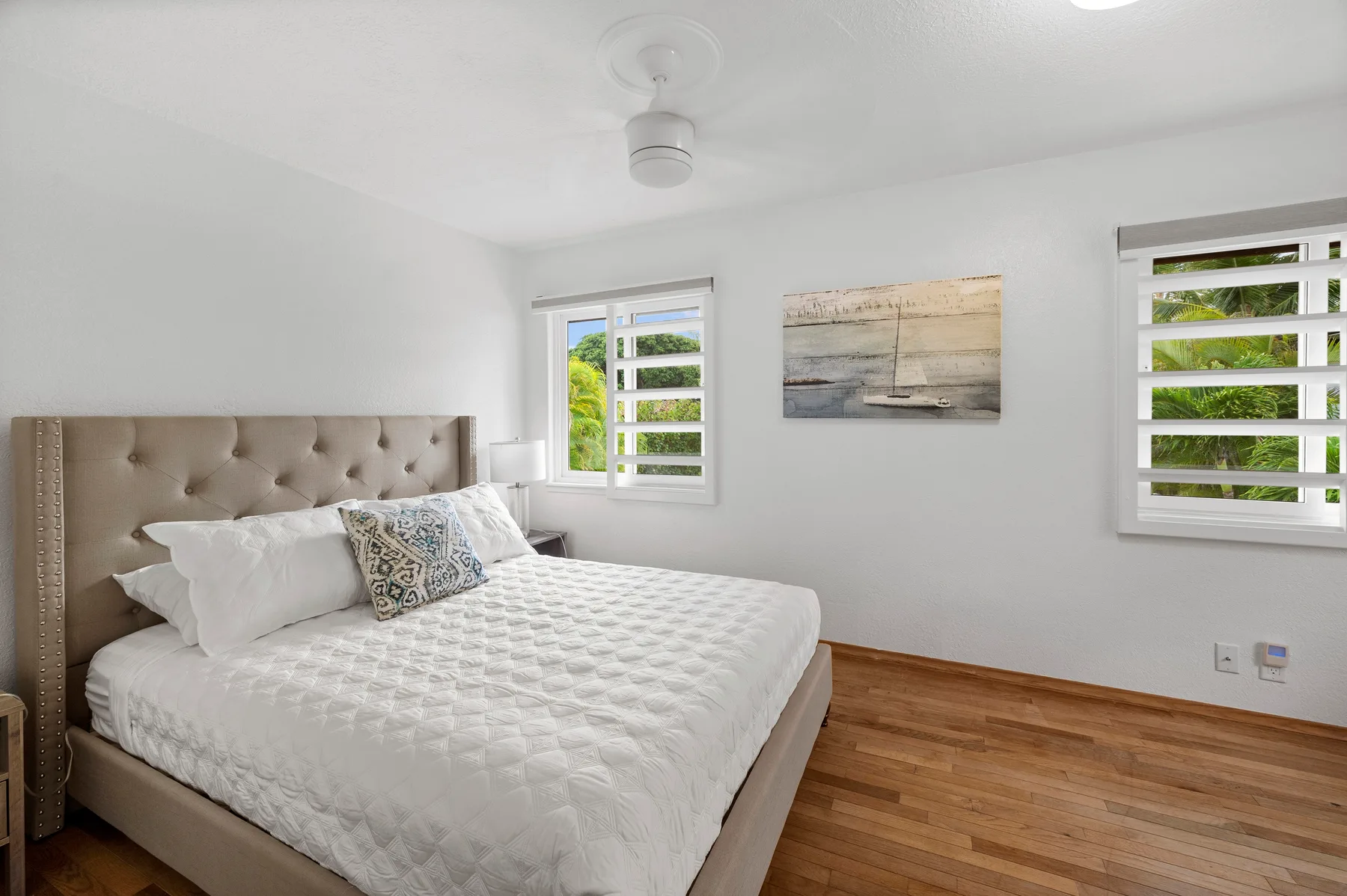 A bright bedroom with a large bed and two windows.