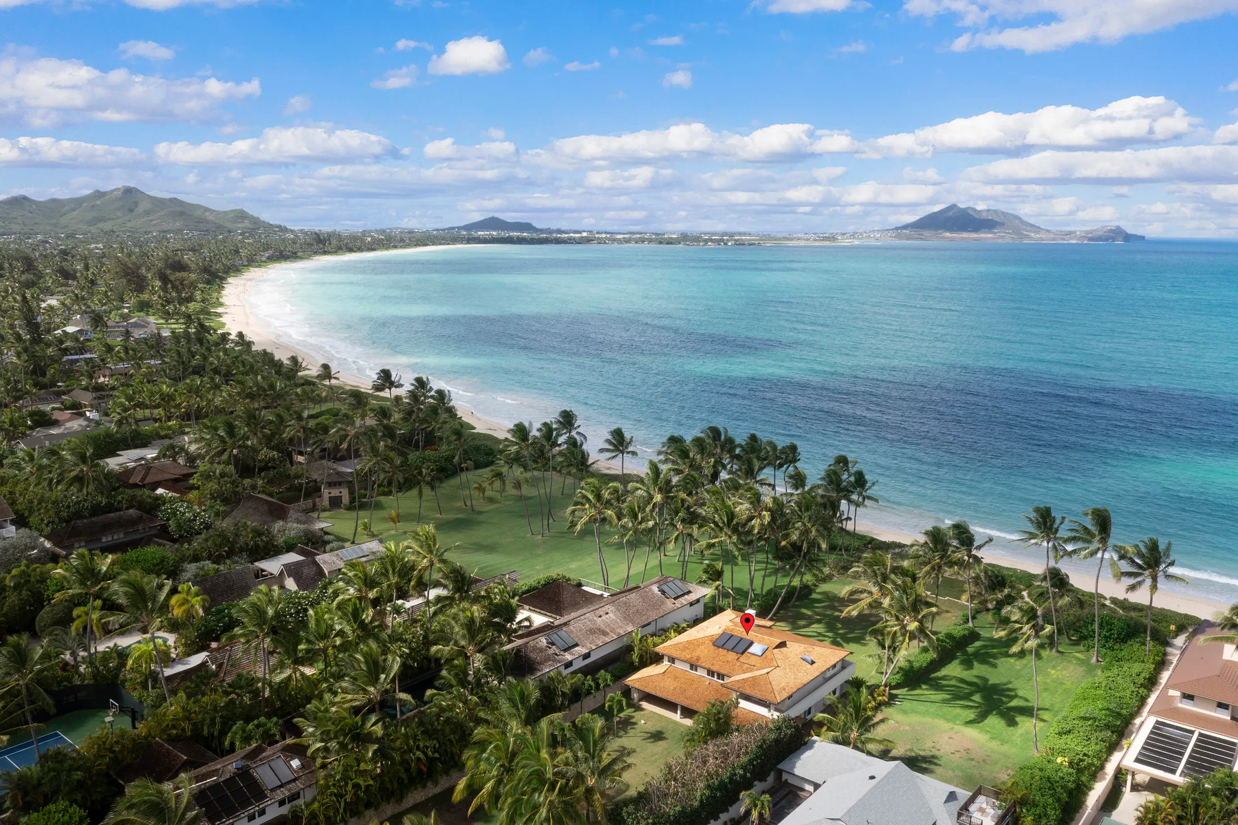 Aerial view of a tropical coastline with a curved beach and palm trees.
