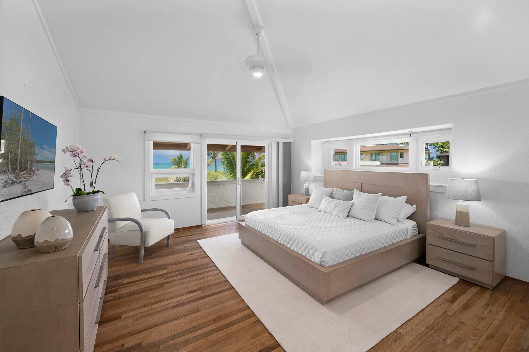 A bright bedroom with a large bed, bedside tables, and windows opening onto greenery.