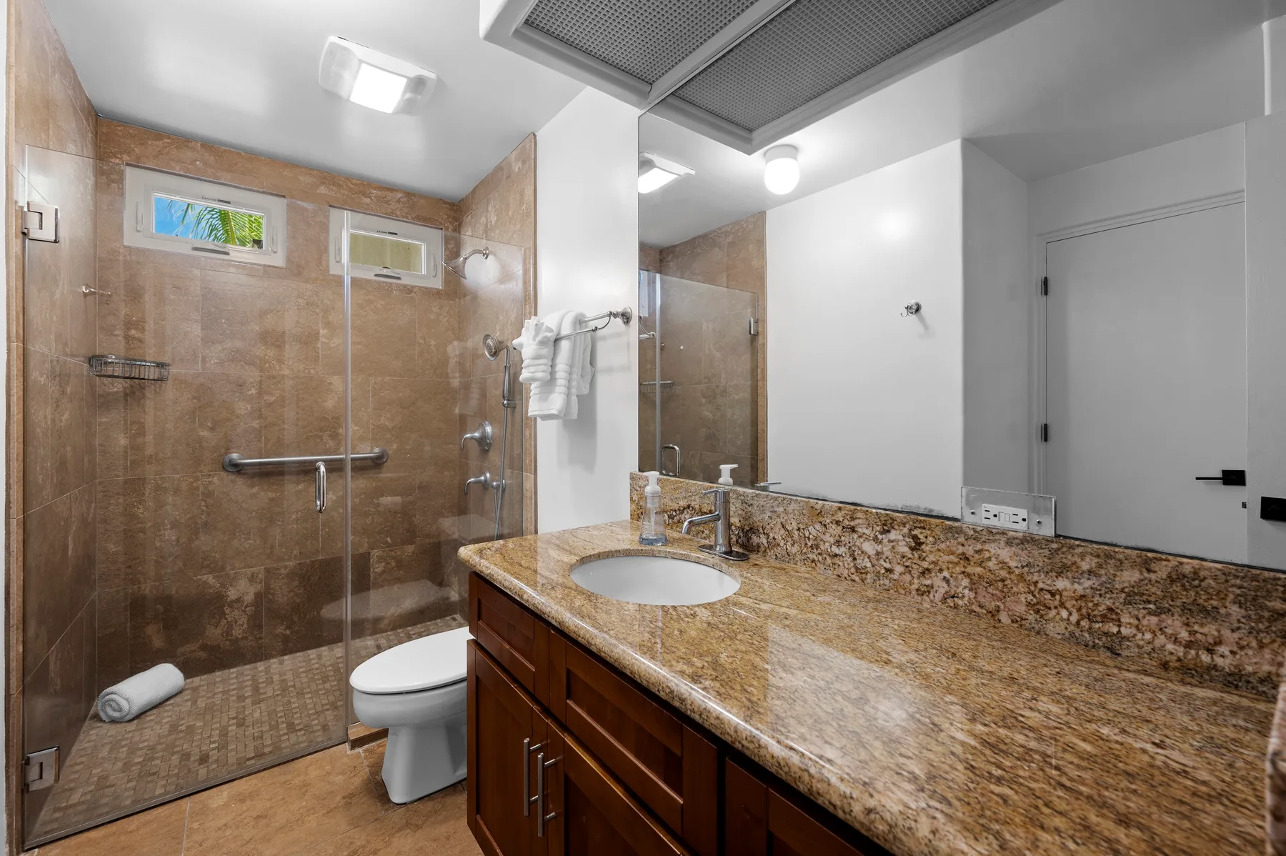 A bathroom with a glass shower, toilet, and long vanity with a sink.