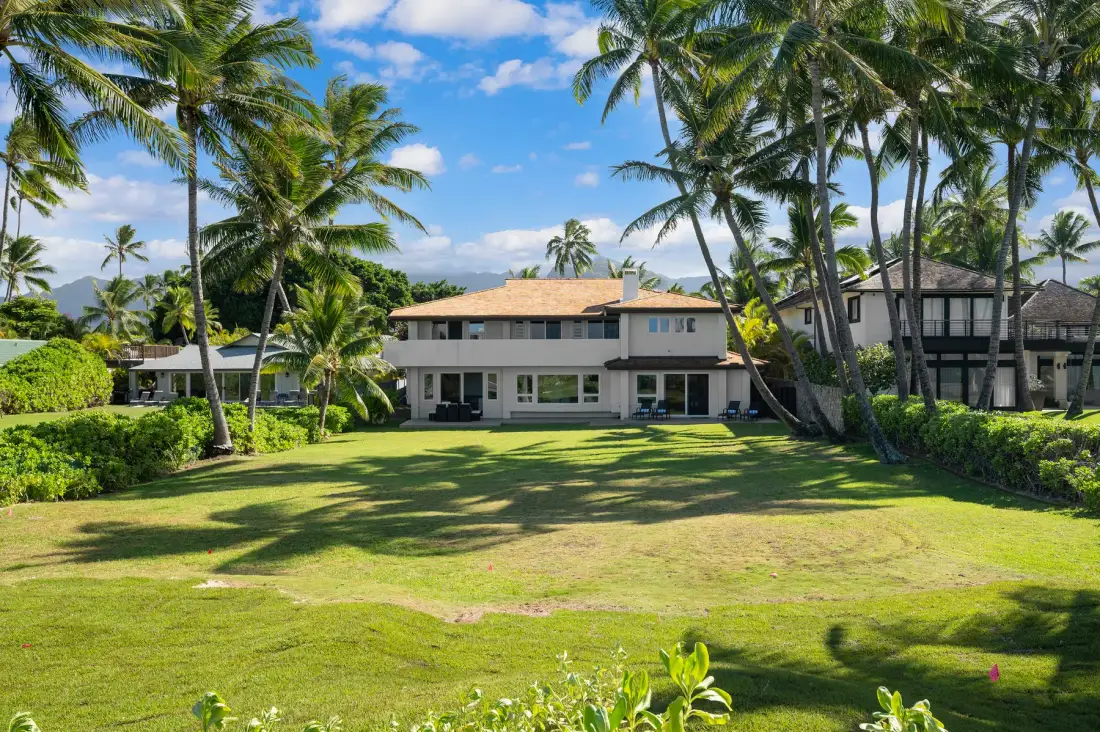 A large house stands beyond a broad lawn, framed by palm trees.
