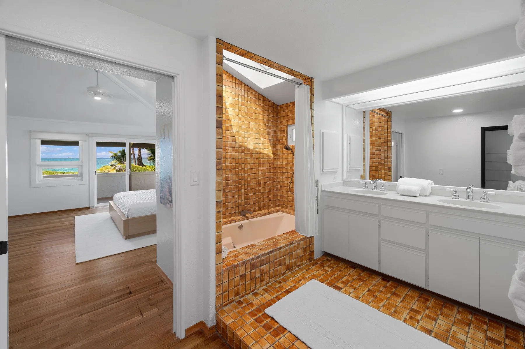 A bathroom with a tiled bathtub, vanity, and a view into a bedroom.