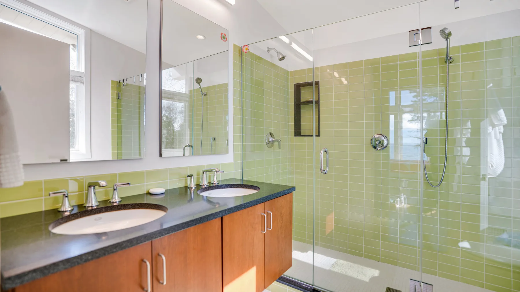 Un baño luminoso con un lavabo doble y una ducha con mampara de vidrio.