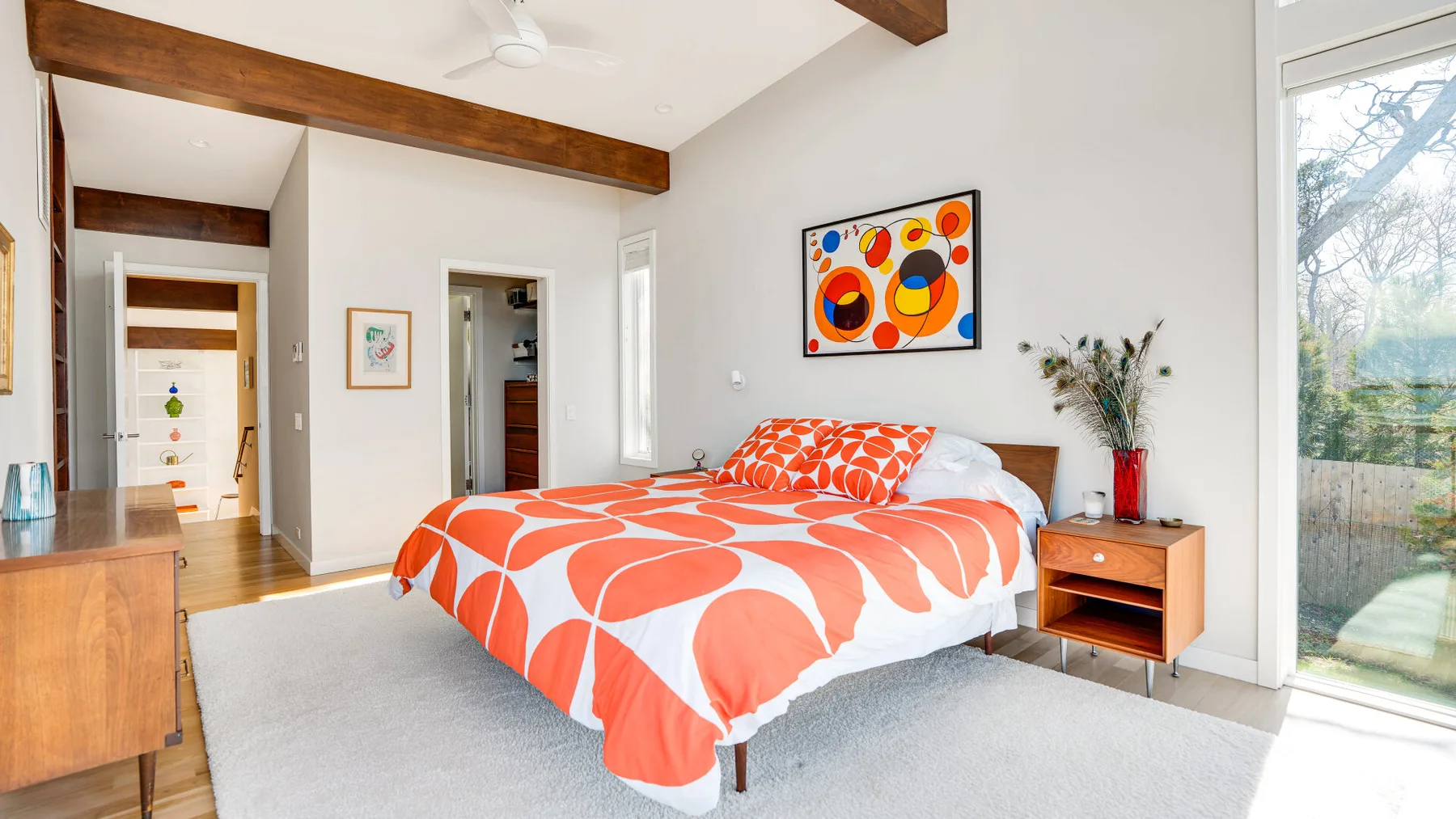 Un dormitorio luminoso con una cama vestida con ropa de cama estampada en naranja y blanco.