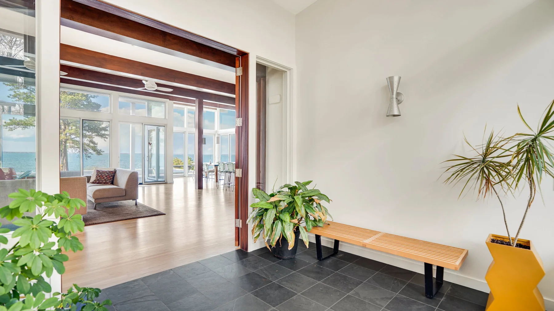Una entrada interior luminosa se abre a una zona de estar, con un banco de madera junto a la pared.