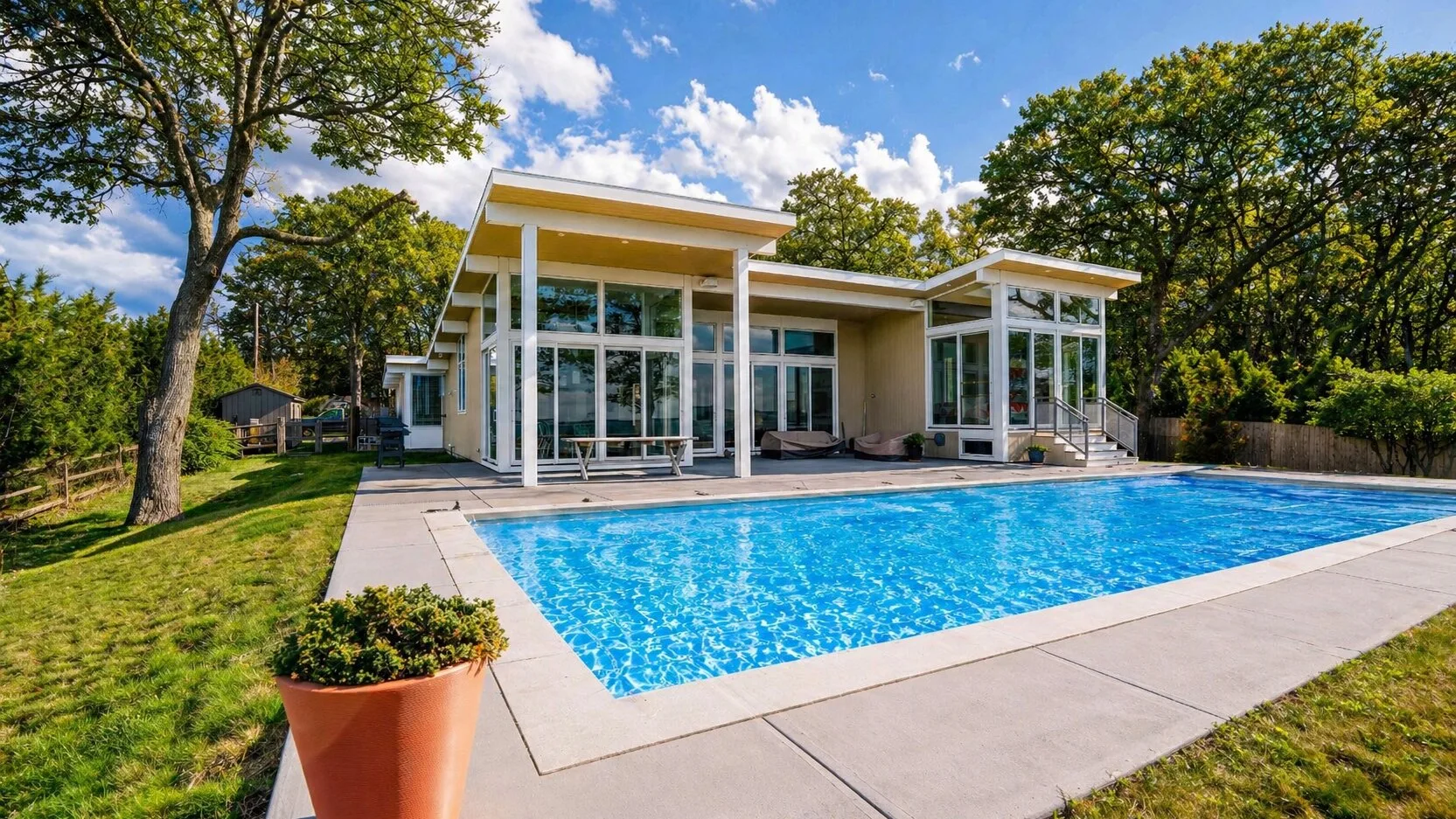 Una casa moderna da a una piscina, con árboles alrededor del jardín.