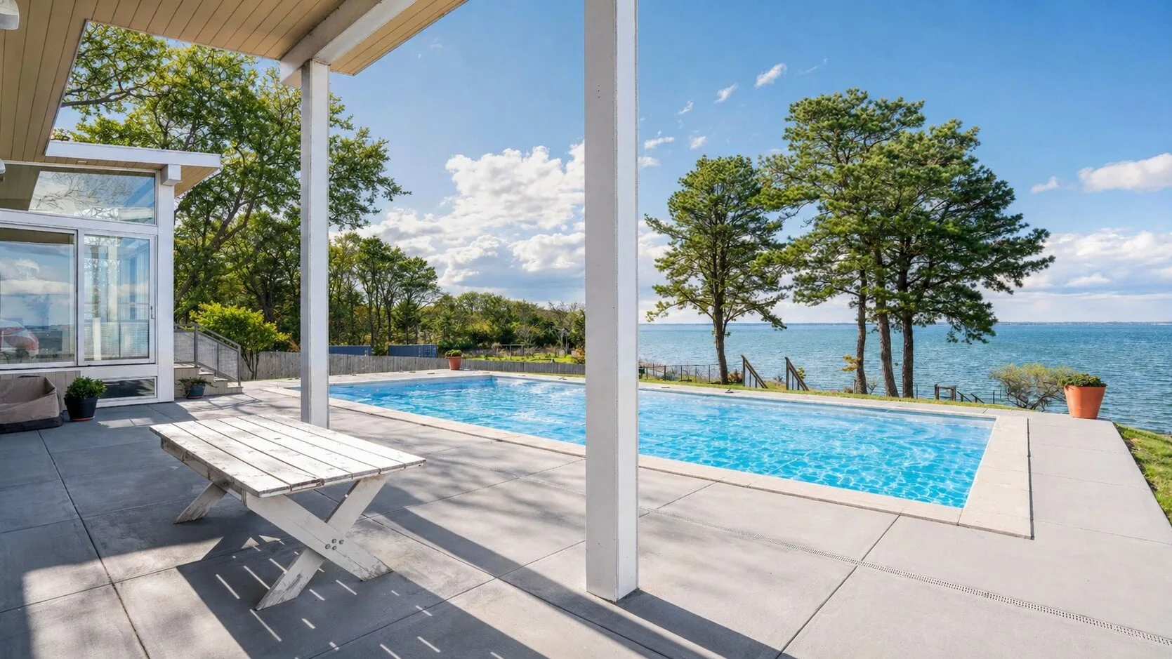 Un patio cubierto da a una piscina y al agua más allá.
