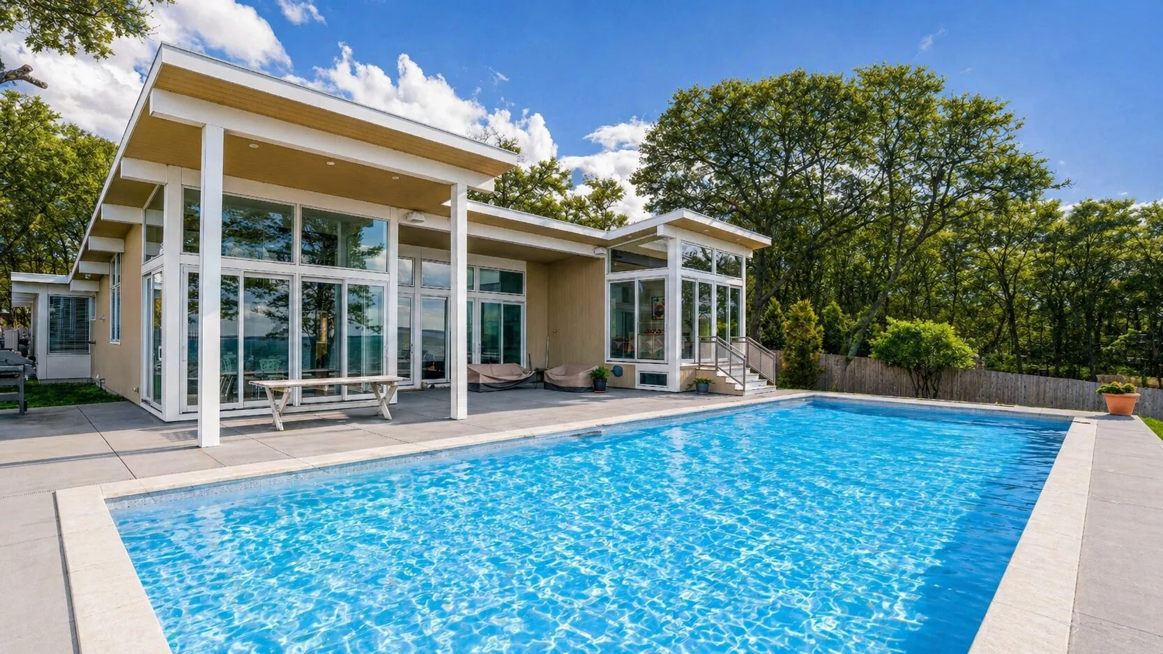 Una casa moderna con una gran piscina exterior bajo un cielo azul.