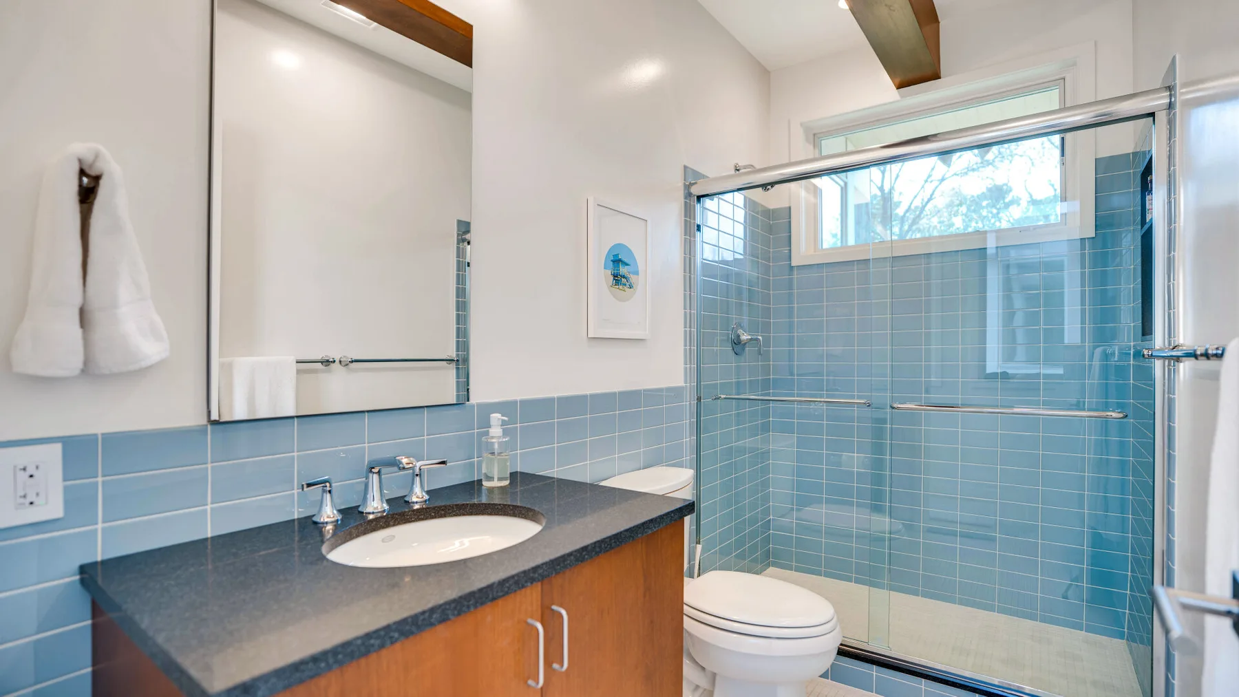 Un lavabo de baño está junto a una ducha de vidrio con azulejos azules.