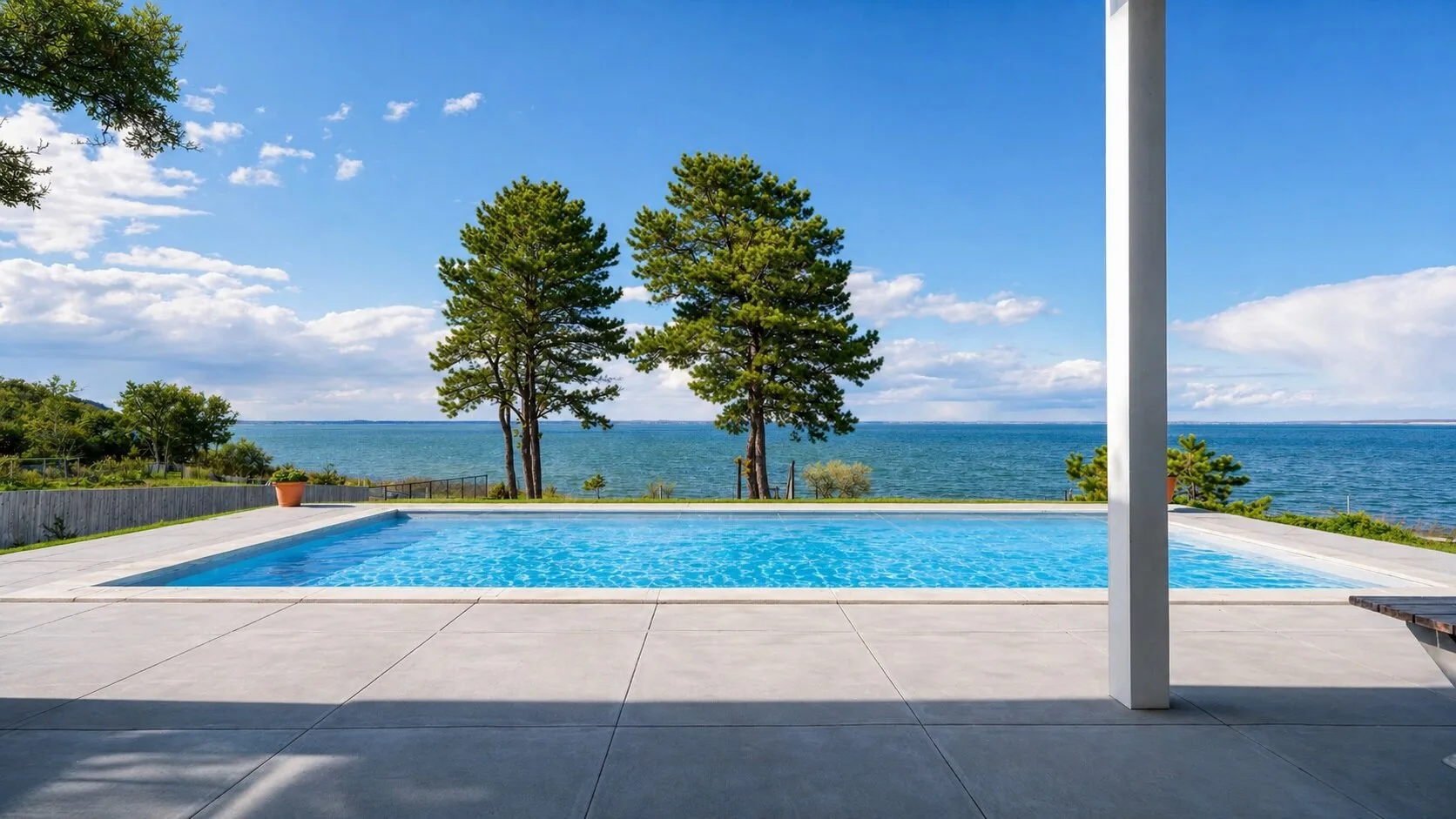 Una piscina y una terraza pavimentada dan al mar bajo un cielo azul despejado.