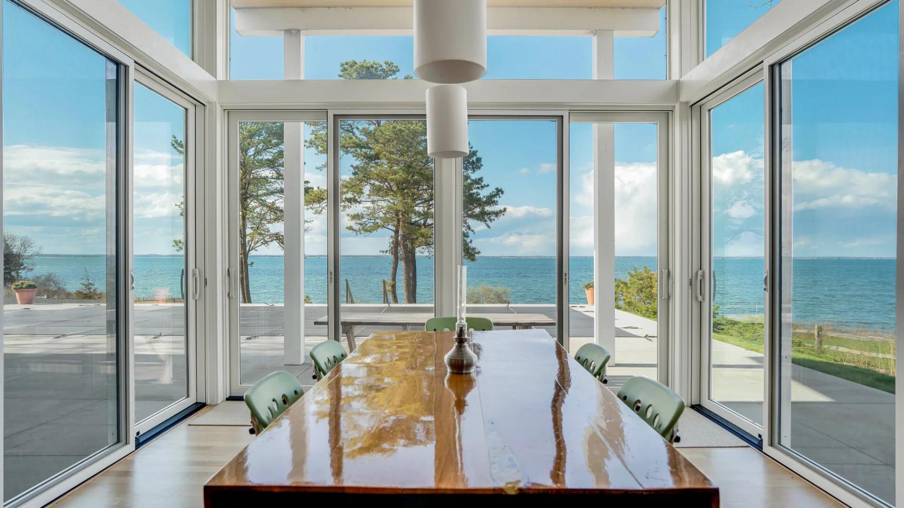 Un comedor con una mesa larga de madera junto a ventanales con vistas al agua.