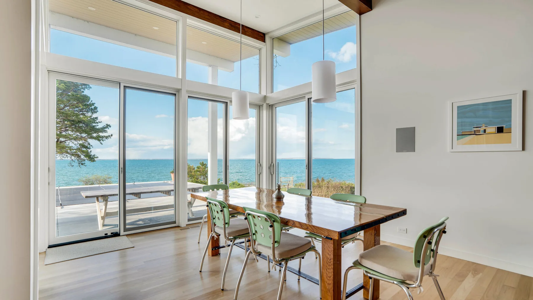 Comedor con una mesa de madera y grandes ventanales con vistas al agua.
