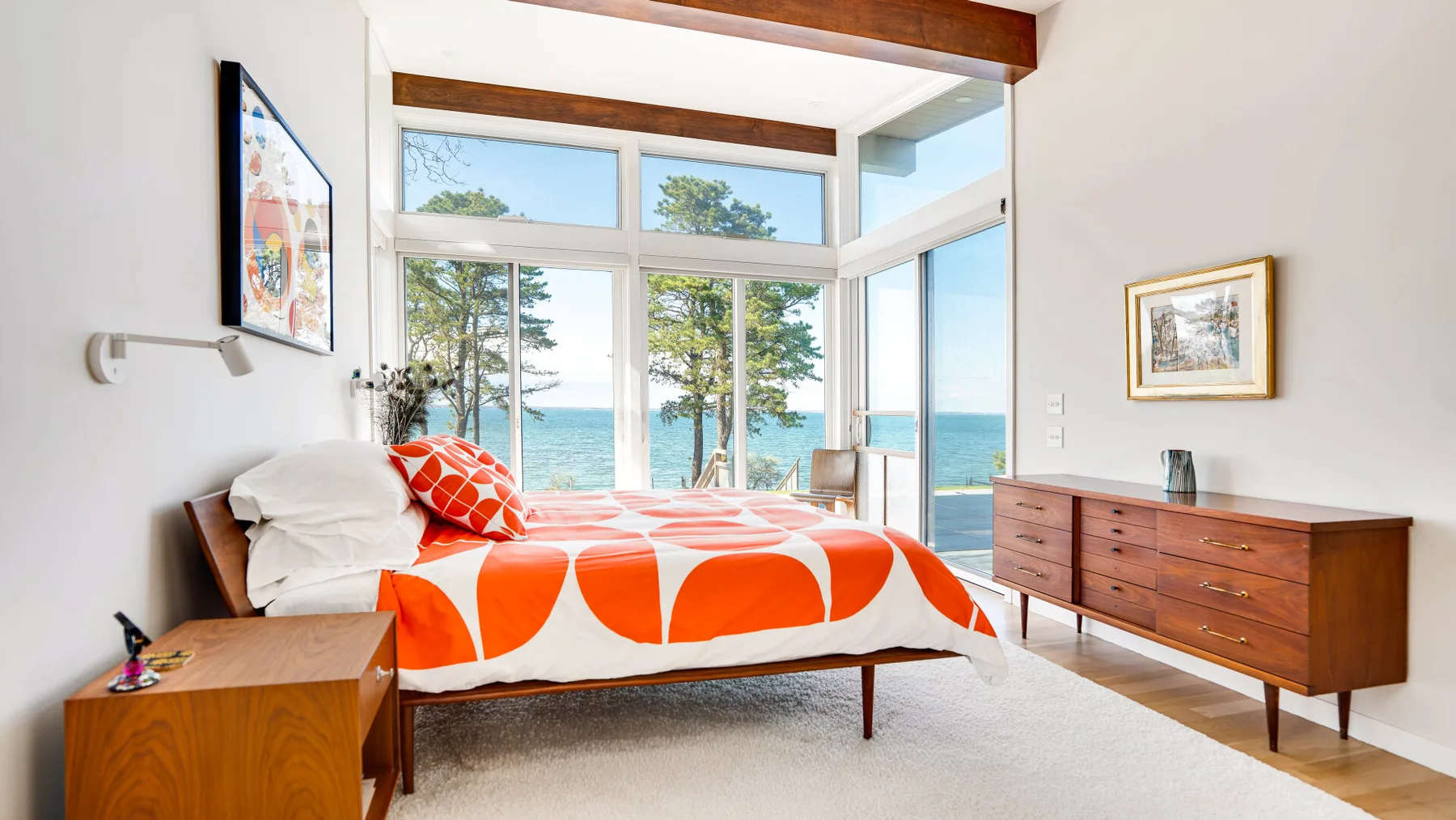 Un dormitorio luminoso con una cama junto a grandes ventanas con vistas al agua.
