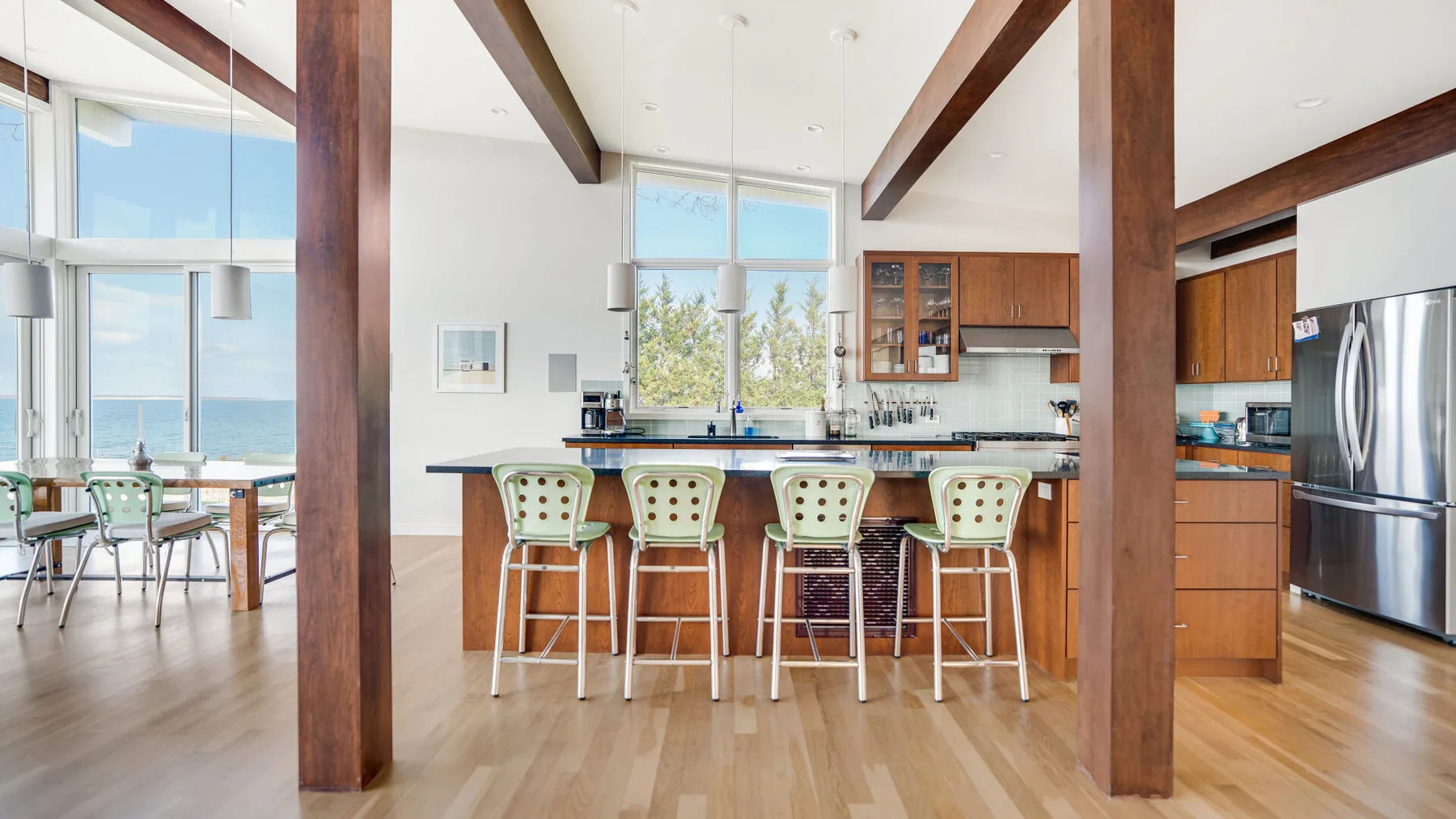 Una cocina abierta con comedor tiene una isla grande con asientos y ventanas altas.