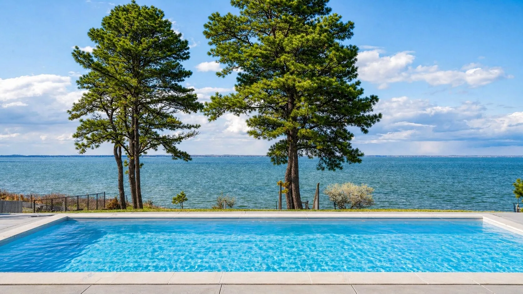 Una piscina al aire libre junto a un lago, con árboles junto al agua.