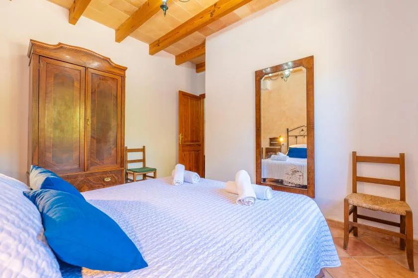 A bedroom with a bed, wooden wardrobe, and mirror.