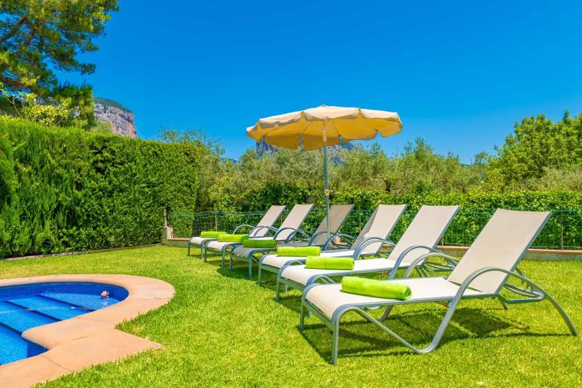 Outdoor poolside seating with loungers and a sun umbrella on a grassy lawn.