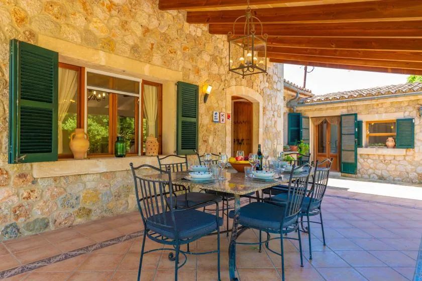 A covered stone patio with a dining table and surrounding seating.