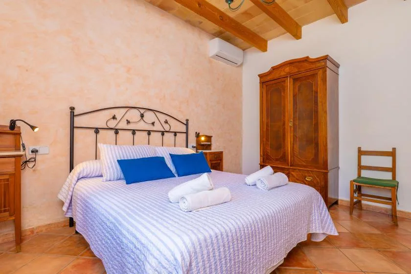 A bedroom with a double bed, wooden wardrobe, and exposed ceiling beams.