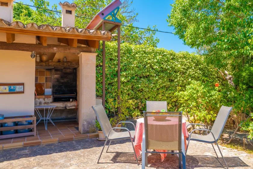 A patio seating area beside a covered outdoor kitchen, surrounded by leafy greenery.