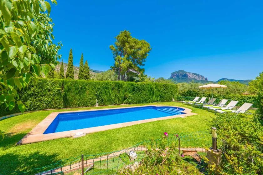 An outdoor swimming pool sits in a green garden with loungers and a parasol.