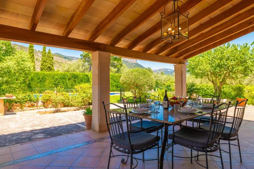A covered outdoor dining area with a table and chairs overlooking a garden.