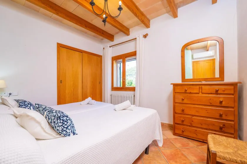 A bedroom with a bed, wooden dresser, and exposed ceiling beams.