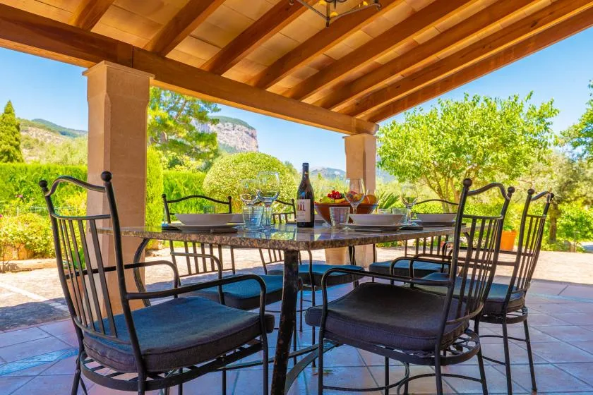 A shaded outdoor dining area with a table and seating beneath a wooden pergola.